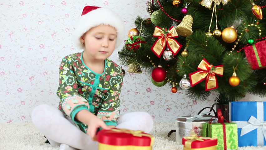 Child in Santa cap tosses confetti and sitting on the floor near a Christmas