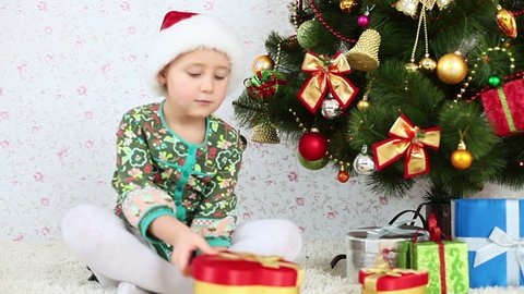 Child in Santa cap tosses confetti and sitting on the floor near a Christmas tree