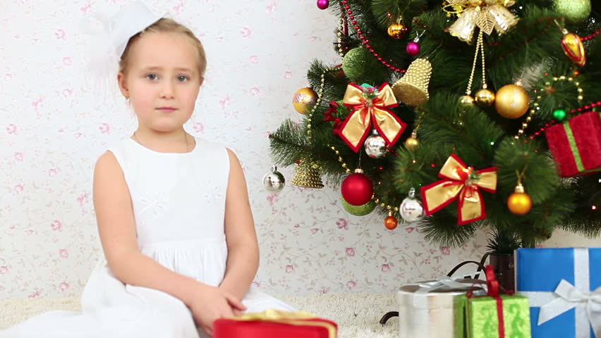 Girl tosses confetti and sitting on the floor near a Christmas tree