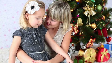 Mother kisses her daughter sitting on the floor near the Christmas Tree