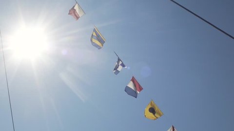 Slow motion shot of the nautical flags fluttering in the wind against blue sky with sun