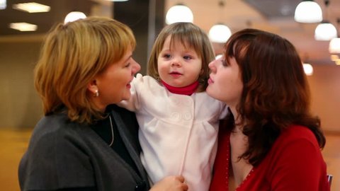 Grandmother and young mother kiss little girl inside cafeteria