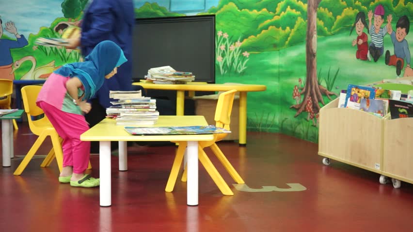 Asian Muslim mom wearing headscarf helping kids reading books, and finishing homework in a children library corner.