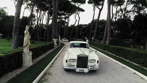May 2015  White Rolls Royce walking down the street surrounded by greenery. Aerial drone N.
Videos about marriage, ceremony, decorations, wreaths, garden,wedding, rolls royce, car,  luxury, lust,