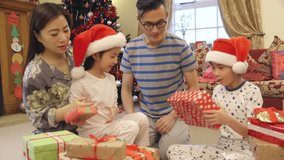 Chinese family on Christmas morning. The children are sitting on their parents laps, shaking the wrapped presents to try and work out what is inside. - Powered by Shutterstock - Get 15% off with code: PIKWIZARD15