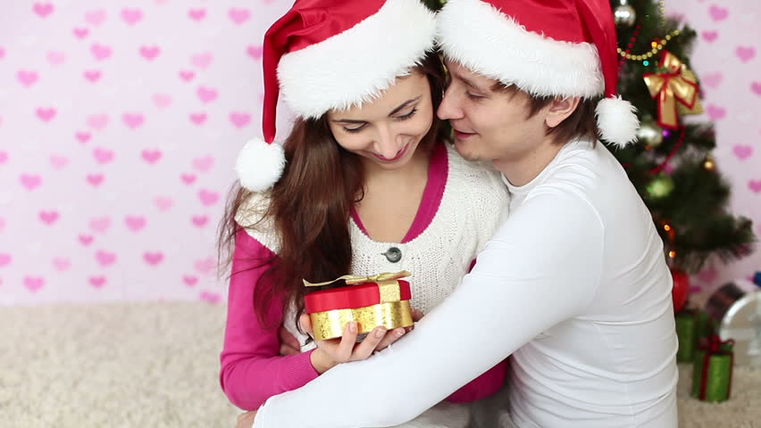 Girl opens the gift and laughs. Couple in love sitting near a Christmas tree