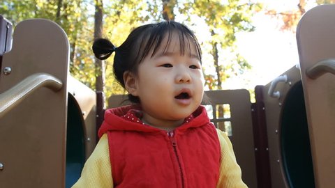 Asian Baby Toddler Girl in Red Vest Babbling on Playground