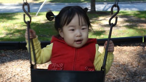 Asian Baby Toddler Girl in Red Vest Swinging in Swing
