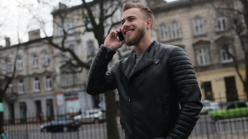 Smiling man talking on his phone while standing in the street.