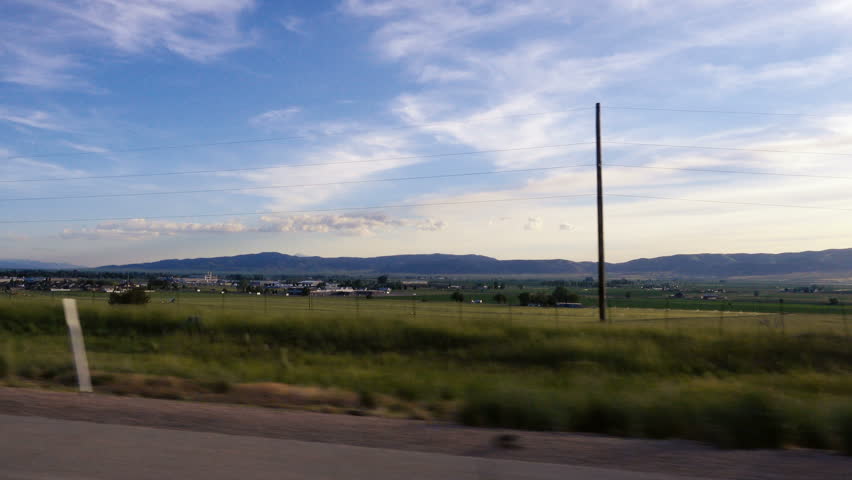NEPHI, UTAH - MAY 30, 2016: Point of View-Passenger side window passing farms and green fields with power lines and the outskirts of the town of Nephi, Utah in the back ground.