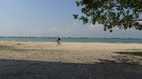 , Singapore-13 April, 2015: 4k, A fisherman walking in the beach with background of cargo ships containers sailing at east coast park of Singapore-Dan