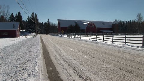 Car drives down plowed road past barns and snowy field