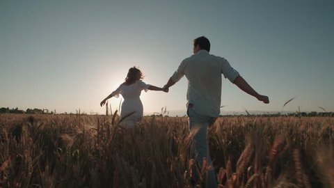 Happy, young couple running across the wheat field,sunset light, summer season.High speed camera,slow motion
