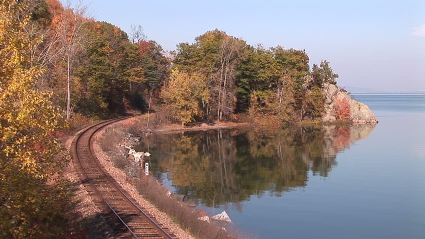 Railroad track emerges from autumnal forest and curves alongside lake