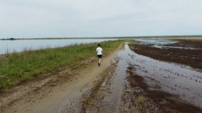 Boy runs a country road along the shore of the bay. Steady shot, 4K video.