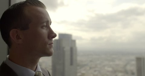 Handsome young business man looks across Los Angeles from Downtown office window.  Big close up with sunrise sky, dolly shot originally recorded in 4K