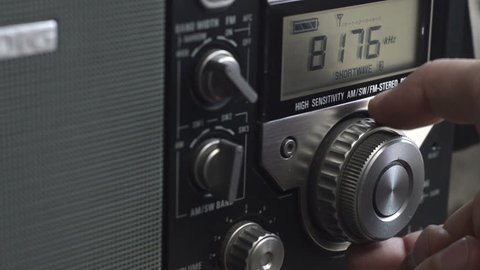 Tuning radio station. Hand of man turning dial of a radio and adjusting volume.