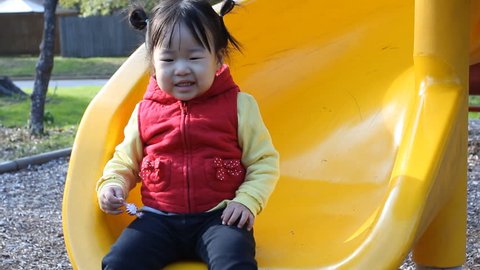 Beautiful Asian Baby Toddler Girl on Yellow Slide in Playground