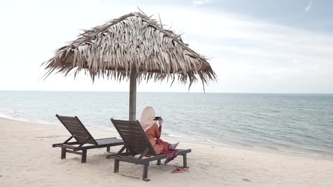 Woman resting at a wooden lounge watching beautiful beach and strong wind blowing at Batu Buruk Terengganu Malaysia. HD ungraded log footage.