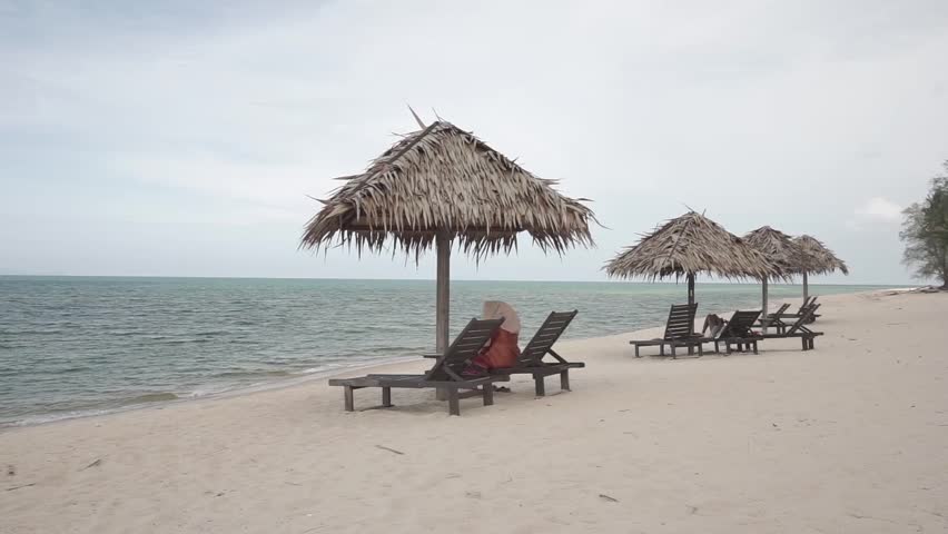 Woman resting at a wooden lounge watching beautiful beach and strong wind blowing at Batu Buruk Terengganu Malaysia. HD ungraded log footage.
