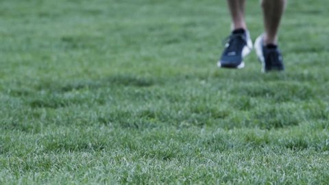 A close-up shot of a man's legs running through a field in 240 frames per second, slow motion. New York - May 1, 2016