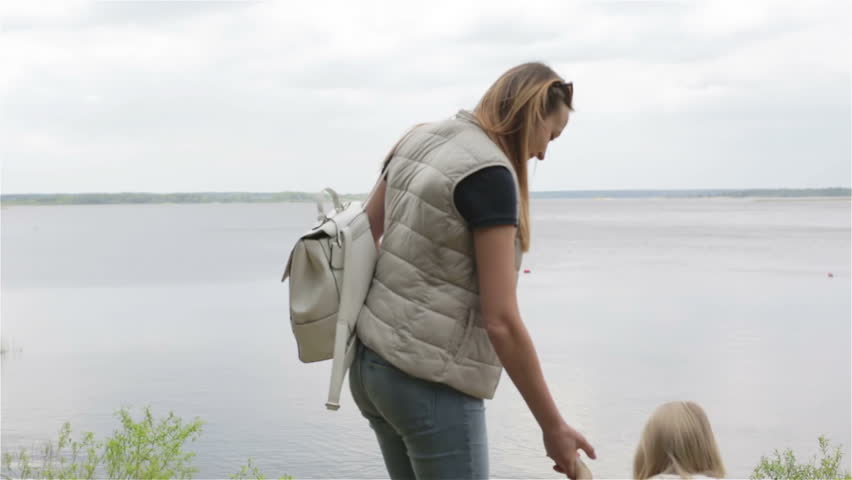 Pregnant woman and small girls are on the beach of a forest lake. Mom and daughter are going down to the water. Family stroll outdoors.