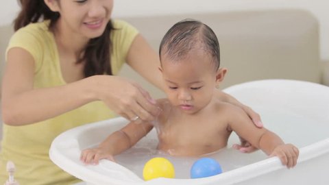 portrait of a baby having a bath by his mother using tub at home