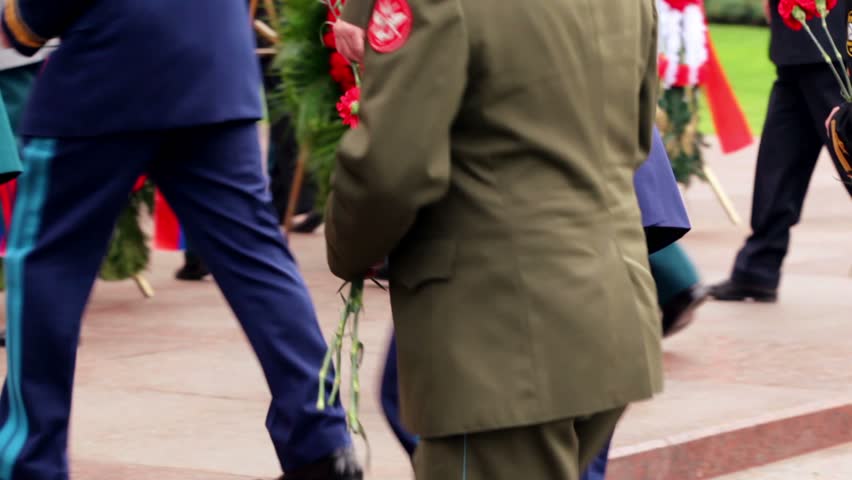 Military men ascend on stairs with red flowers, they put it at monument of Unknown Soldier, on wreath laying ceremony, only legs are visible
