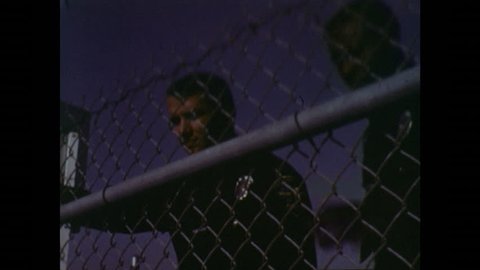 UNITED STATES 1970s: Police Officers Peer Through Fence at Boy Playing Out After Dark