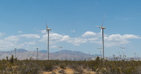 Wind turbines at Tehachapi in Mojave Desert near mountains.  Small clouds pass overhead.  Time lapse clip.