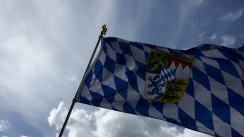 Sun and ray of light behind the waving flag of Bavaria in Germany with a cloudy blue sky in background 