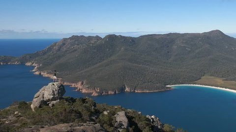 a zoom out view of a hiker looking at wineglass bay from mt amos on the east coast of tasmania, australia
