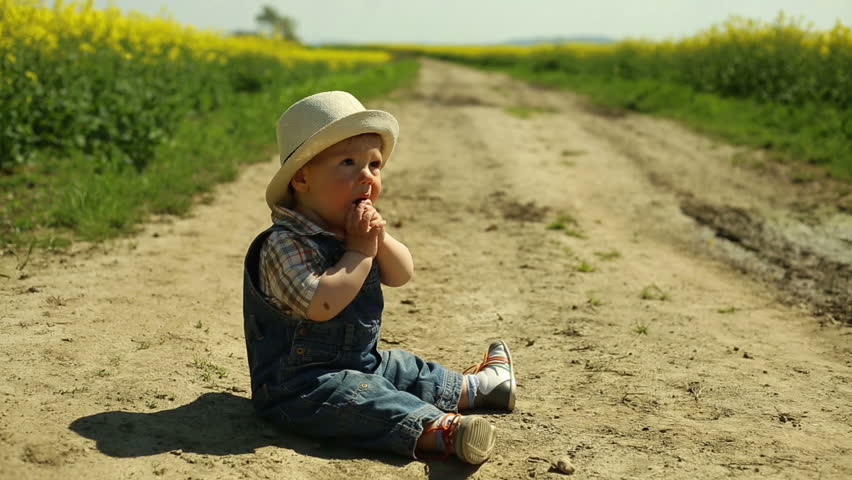 Smiling baby sits on a road at the village
