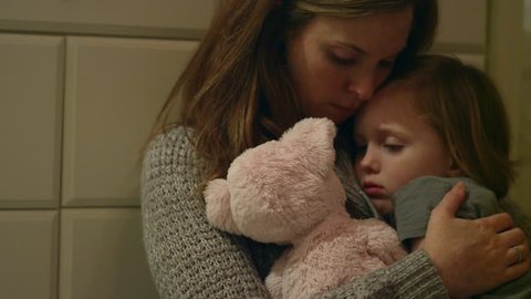 Sad, scared young girl with a stuffed animal being held by her mother in her room