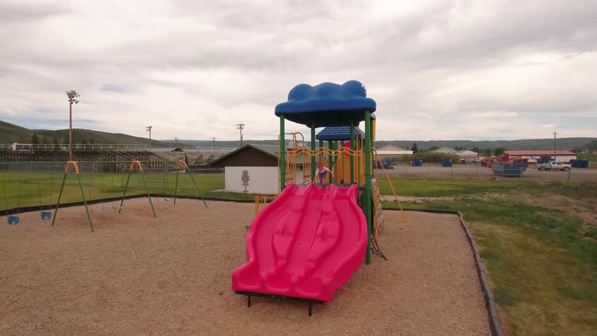 A fun aerial shot of a little boy playing at the town park on the slides and swings