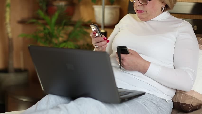 Businesswoman with mobile phone and notebook. Senior woman in glasses with laptop and cell phone. Female with smartphone and laptop sits on a sofa Royalty-Free Stock Footage #17407486