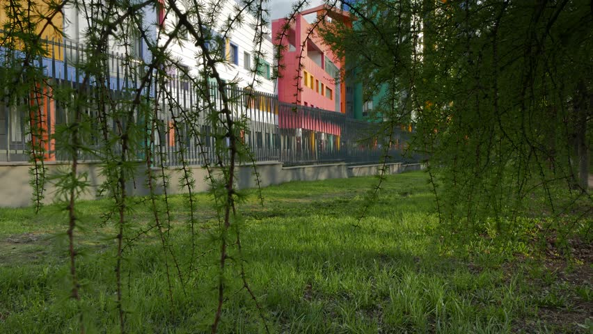 Colored Building of the Dima Rogachev Federal Research Centre of Paediatric Haematology, Oncology and Immunology in Moscow, Russia. View Through a Green Tree Branches With a Woman Passing by Camera.