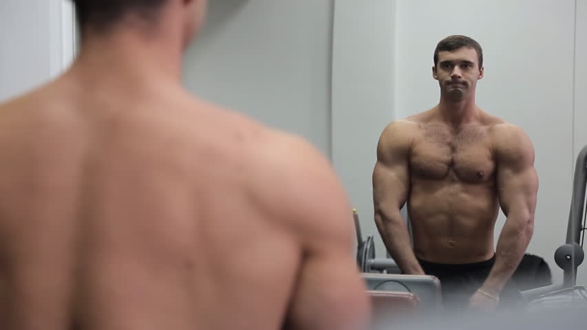Bodybuilder in front of the mirror shows his huge muscles