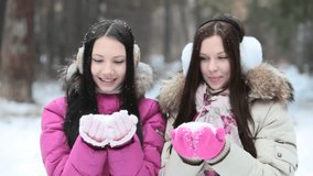 Two girls blowing then throwing snow in front of the camera
