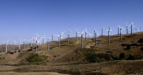 Wide view of lots of wind turbines generating power on a hillside at a wind farm near the Tehachapi Mountains in California.  Clear blue sky.
