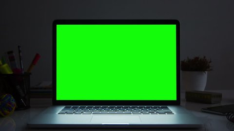 Laptop with green screen. Dark office. Dolly in. Perfect to put your own image or video. Track with perspective corner pin.   