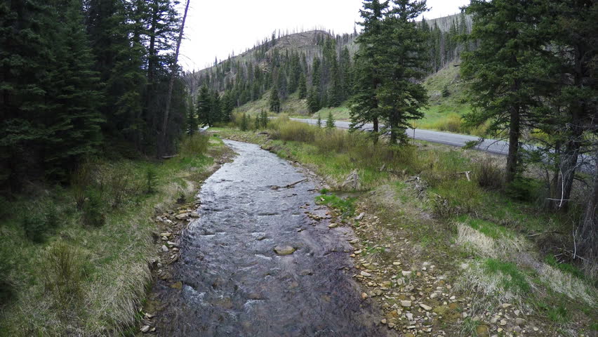 HUNTINGTON CANYON , UTAH - MAY 2016: Aerial-Flying low over beautiful crystal clear mountain stream between brush and pine trees on the banks with forest service road parallel to the stream.
