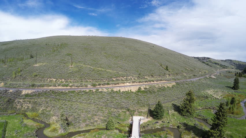 MANTI-LASAL NATIONAL FOREST, UTAH - MAY 2016:Aerial- High altitude view of a mountain meadow with a pole fence and bridge over a lazy meandering stream-pull back