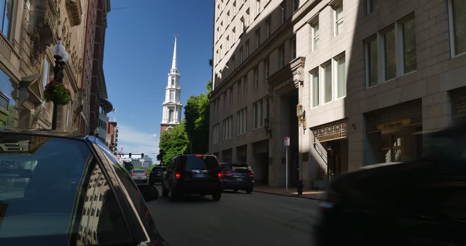 A daytime establishing shot of traffic on Tremont Street in Boston with the Park Street Church in the background.  	