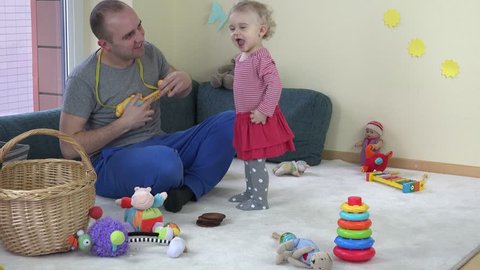Father man play with toy guitar and happy toddler daughter girl dance at home. Static shot.