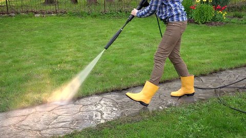 female worker clean dirty path with special tool. Pretty woman in rubber boots work in garden.