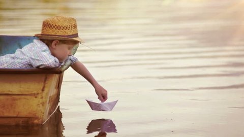 Boy places a paper boat on the water's surface and blows for it to sail away