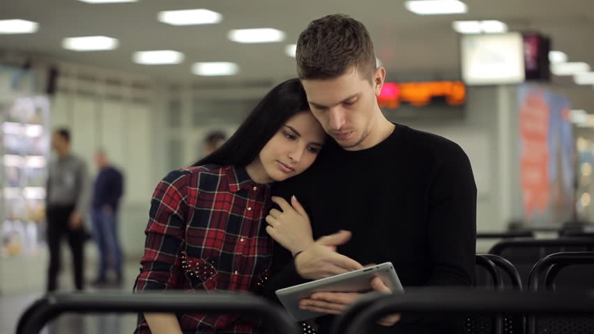 Handsome couple of people sits in departure lounge in airport.