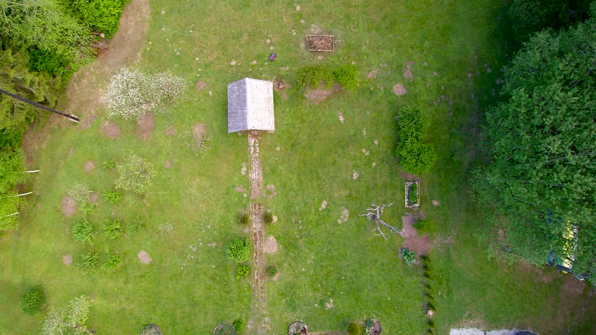 Aerial of the small cabin in the yard with lots of trees around and green grasses