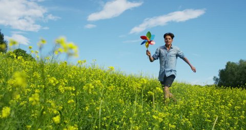 in a day of sun and wind, a happy nice beautiful kid in green nature runs with a  colorful pinwheel helped by the energy of fresh wind .
concept of happiness and renewable wind energy.6k resolution